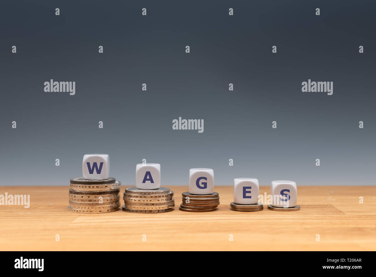 Symbol für sinkende Löhne. Würfel auf Stapel von Münzen bilden das Wort "Löhne". Stockfoto