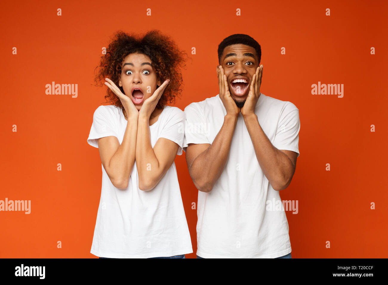 Emotionale afrikanisch-amerikanisches Paar berühren Wangen auf orange Hintergrund Schockiert Stockfoto