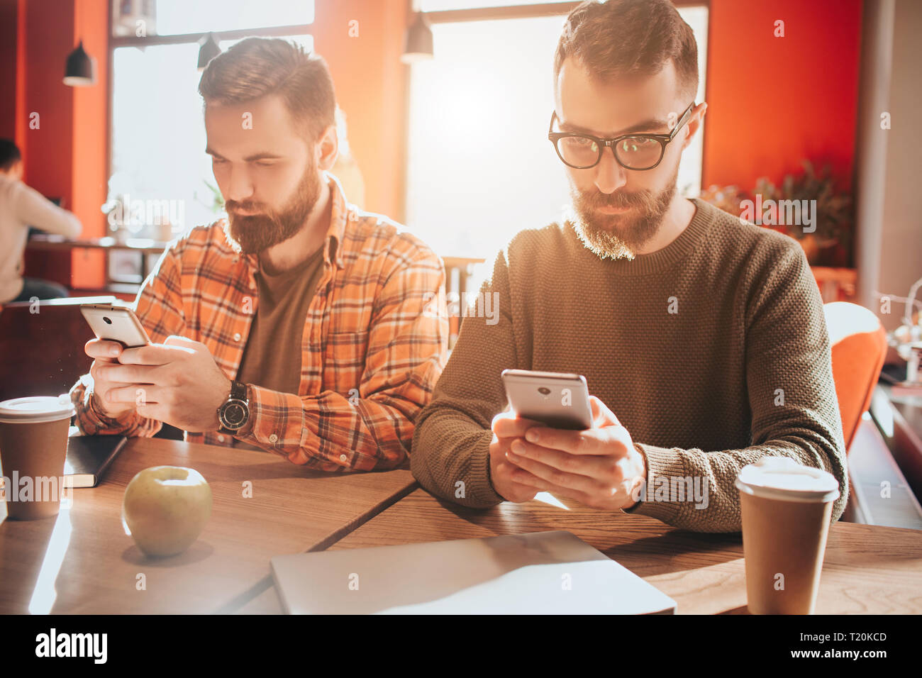 Werfen Sie einen Blick auf Aussehenden bärtigen Männern bei te Tabelle und Telefone. Sie sind nur auf ihren Bildschirmen. Kerle sind besetzt. Schließen Stockfoto
