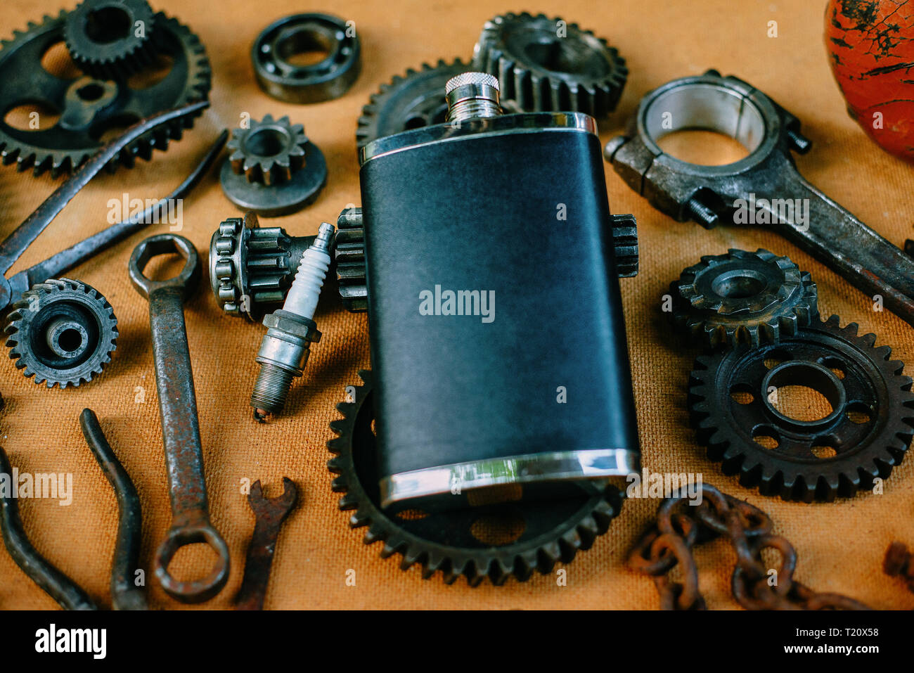 Quadratische schwarze Flasche in der Mitte der rostige Werkzeuge, Zahnräder auf vintage Hintergrund. Motorrad Ausrüstung und Reparatur Vorlage Stockfoto