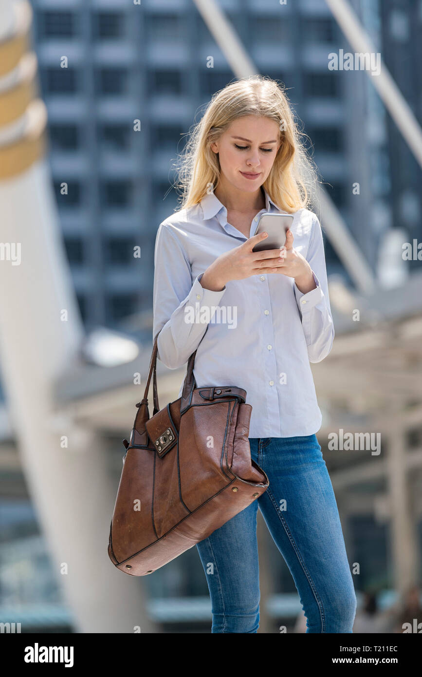 Blonde Frau mit Handtasche prüfen Handy in der Stadt Stockfoto