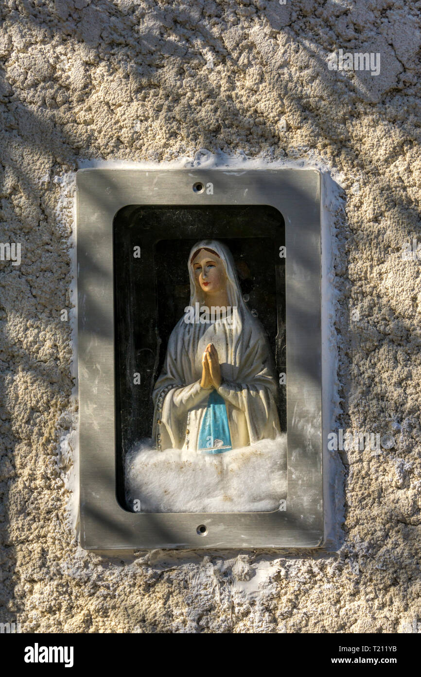 Kleine religiöse Statue der Jungfrau Maria in einer Nische auf der Außenseite eines Hauses in einem französischen Dorf. Stockfoto