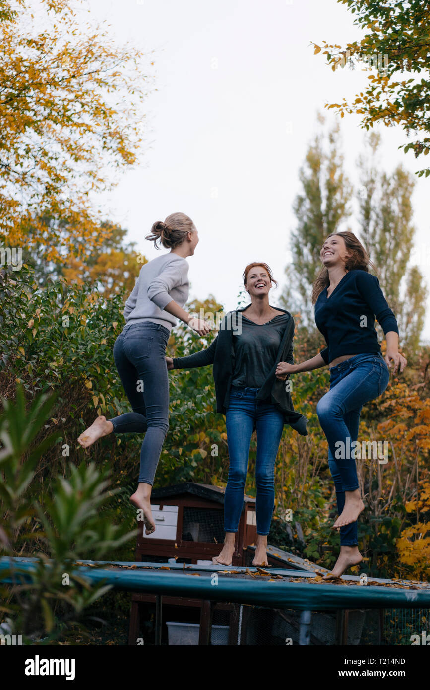 Glückliche Mutter mit zwei Töchtern im Teenageralter springen auf Trampolin im Garten im Herbst Stockfoto