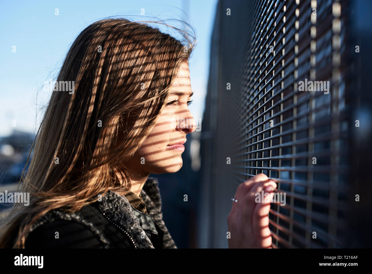 Porträt der jungen Frau mit Schatten auf ihr Gesicht schauen durch Metall Zaun Stockfoto