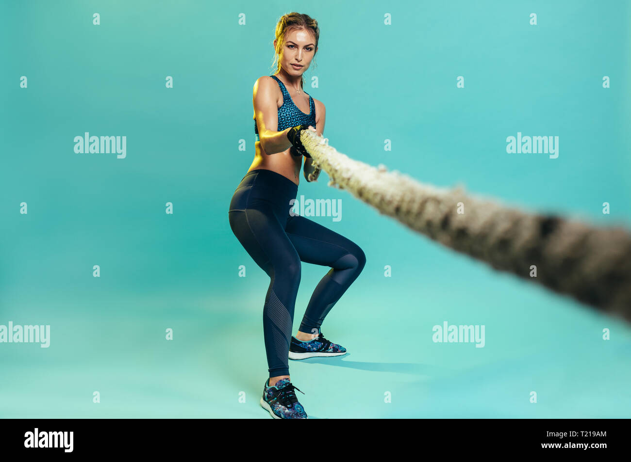 Starken weiblichen Athleten kämpfen, Arbeiten mit Seil im Studio. Gesunde Frau ziehen Schlacht Seil über blauen Hintergrund. Stockfoto