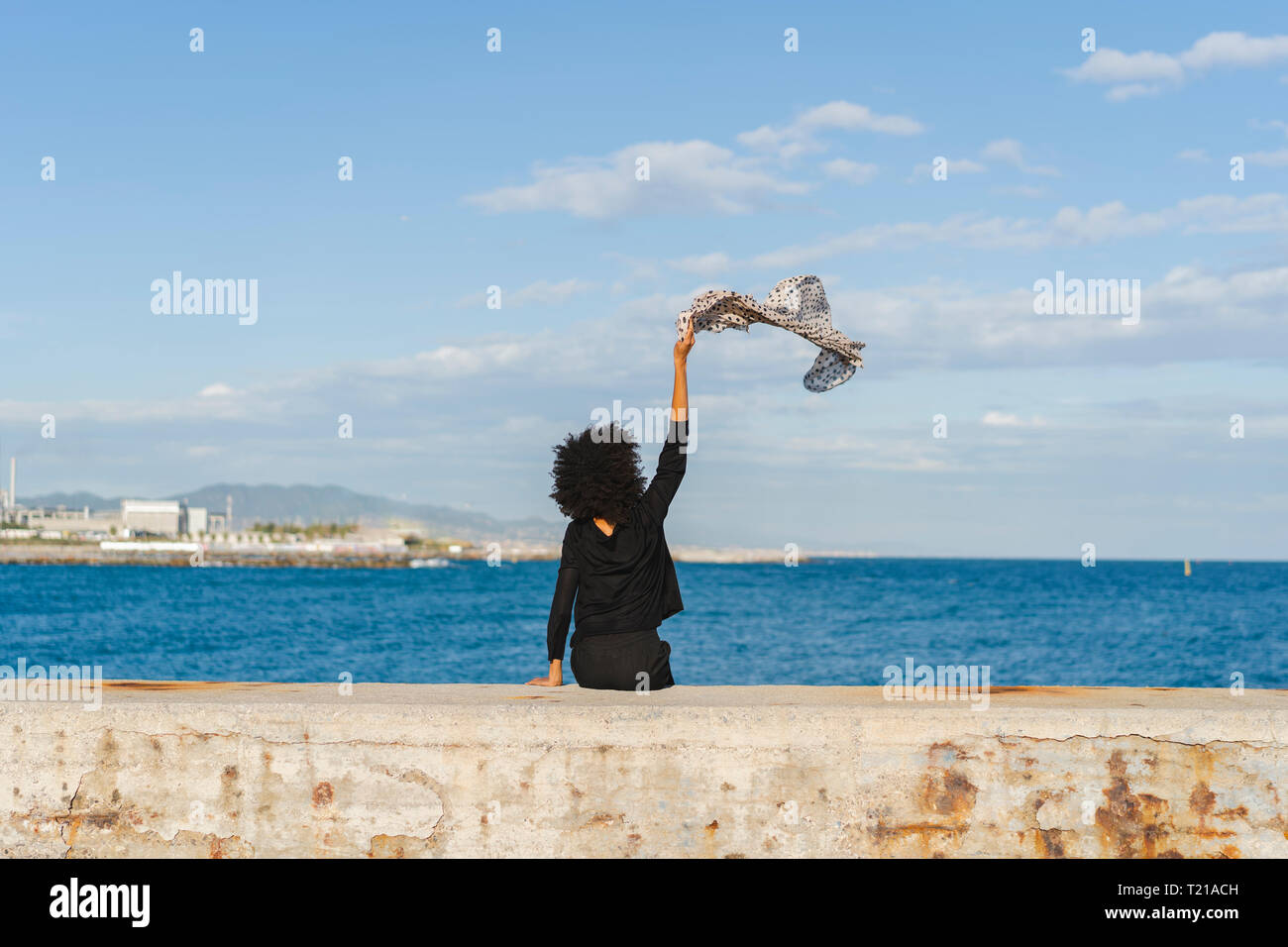 Spanien, Barcelona, Rückansicht der Frau in Schwarz gekleidet, sitzen auf der Mauer winken mit Schal Stockfoto