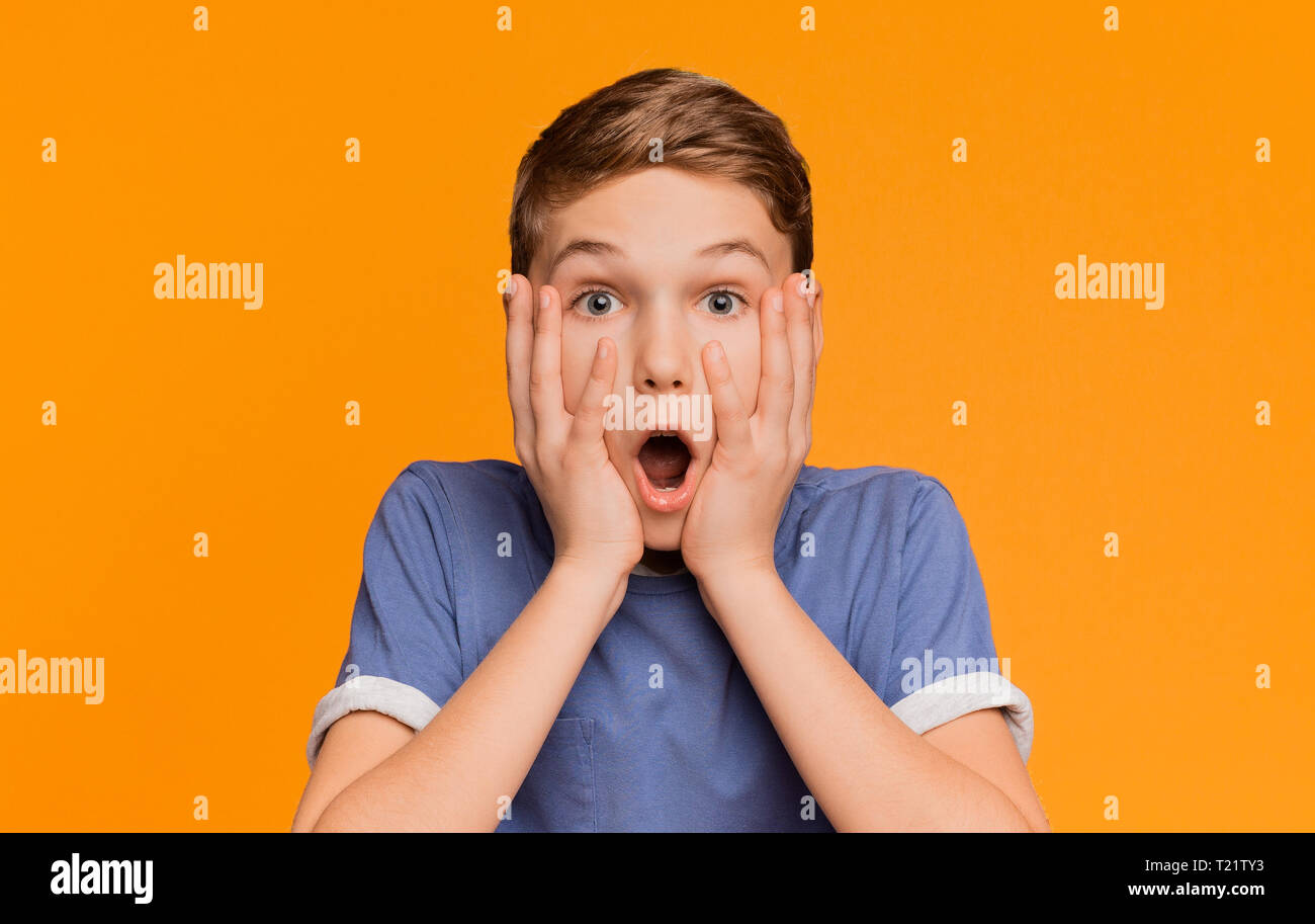 Schockiert Junge öffnete seinen Mund und seine Wangen in Erstaunen, Orange Studio Hintergrund Stockfoto
