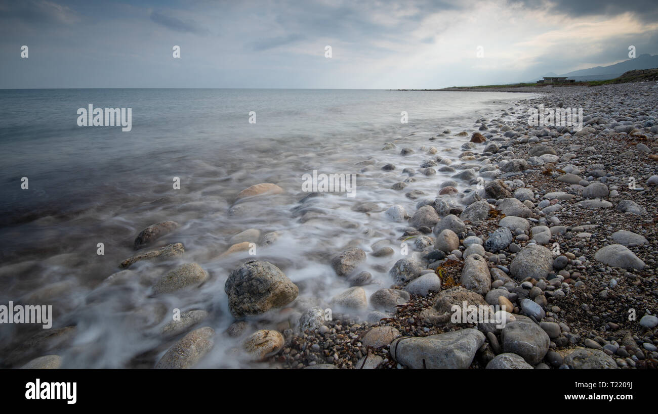 Stürmischen Himmel und welliges Meer mit Wellen schlagen der am Ufer des Meeres voll von schönen und bunten Steinchen. Stockfoto