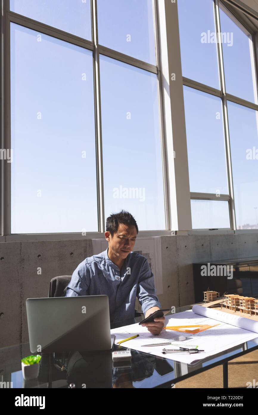 Männliche Architekt am Schreibtisch sitzen und über Handy in modernen Büro Stockfoto