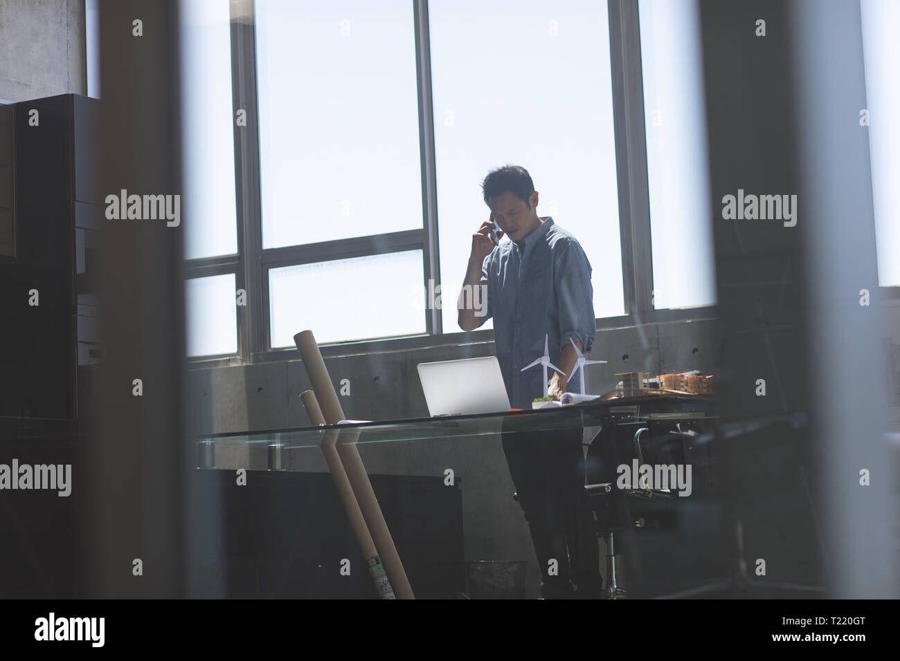 Männliche Architekt stehen und Gespräch am Handy während am Schreibtisch in einem modernen Büro arbeiten Stockfoto