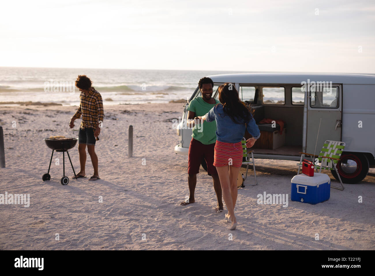 Freunde tanzen zusammen auf Sand am Strand, während eine andere tut ein Grill Stockfoto