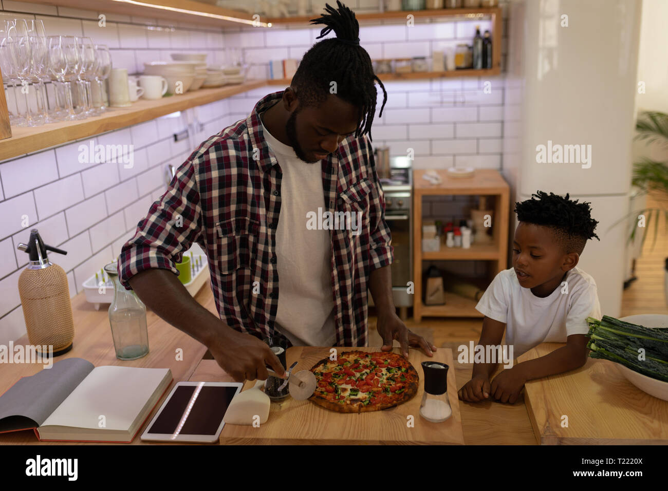 Der Sohn seinem Vater zu beobachten, während die Pizza mit pizza Cutter in der Küche Stockfoto