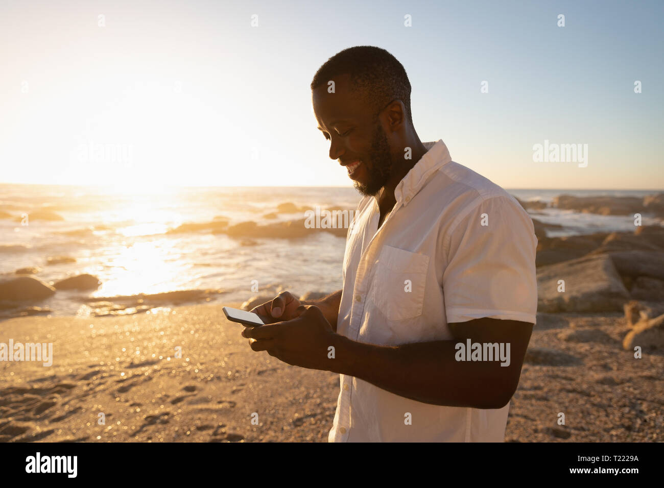 Mann mit Handy am Strand an einem sonnigen Tag Stockfoto