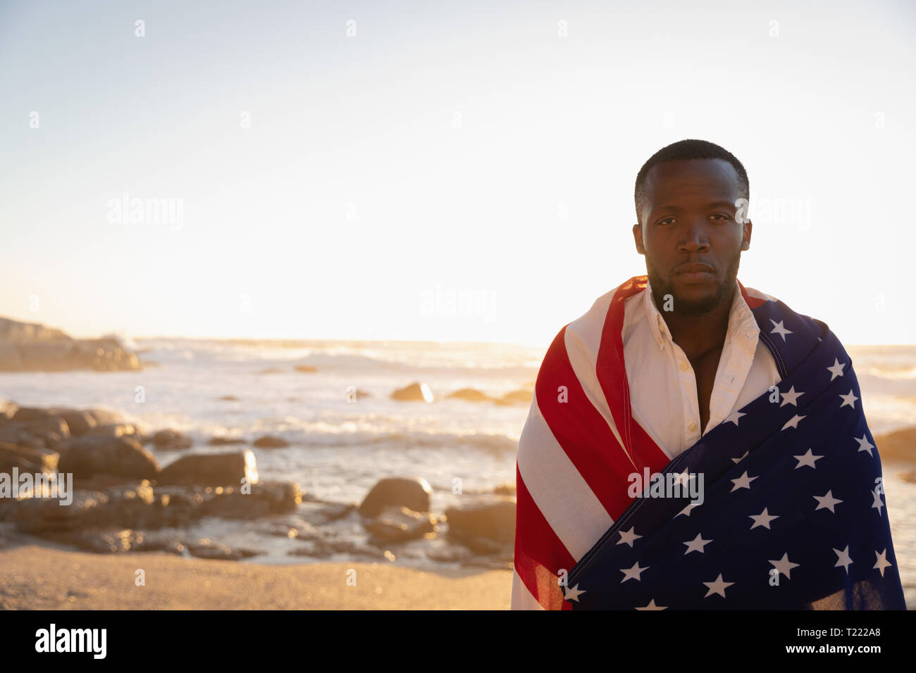 Mann gewickelt amerikanische Flagge beim Stehen am Strand an einem sonnigen Tag Stockfoto