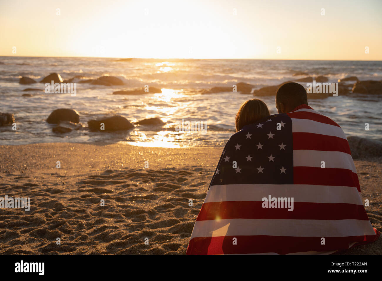 Paar verpackt amerikanische Flagge beim Entspannen am Strand Stockfoto