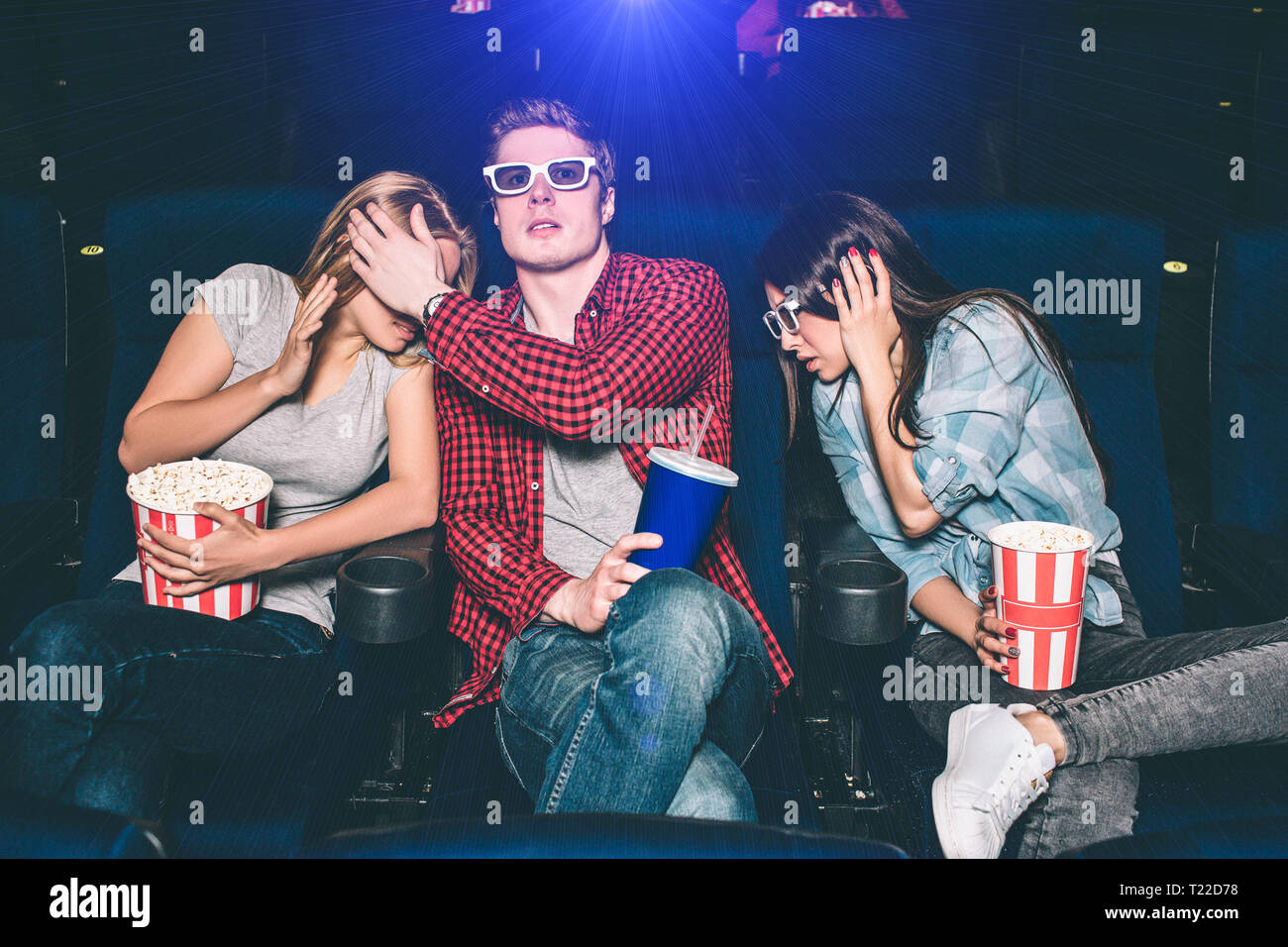 Erschrocken und ängstlich Menschen beobachten Film im Kino. Sie sitzen und gerade nach vorne zu schauen. Jeder hat einen Korb mit Popcorn oder eine Tasse wi Stockfoto