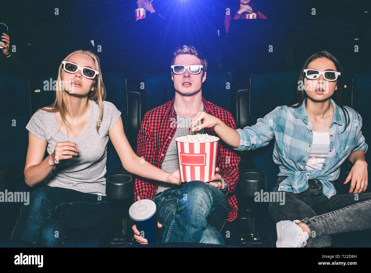 Interestd Menschen beobachten Film im Kino. Thay sitzen und gerade auf der Suche durch spezielle Gläser. Kerl und blonde Mädchen halten eine Box wi Stockfoto
