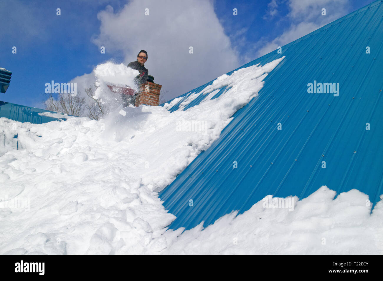 Ein Mann auf dem Dach seines Hauses Schneeräumen in Quebec. Winter 2018-2019 sah sehr starker Schneefall Stockfoto