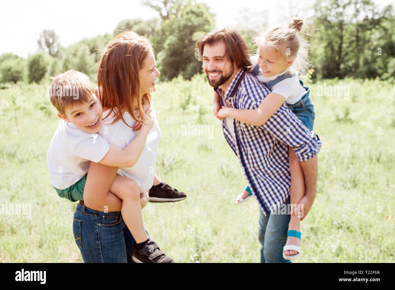 Lustige Momente aus guter Familie. Sie sind draußen auf der Wiese. Eltern sind auf der Suche nach einem Anderen und lächelnd. Sie halten Ihre Kinder auf Ihrem Stockfoto