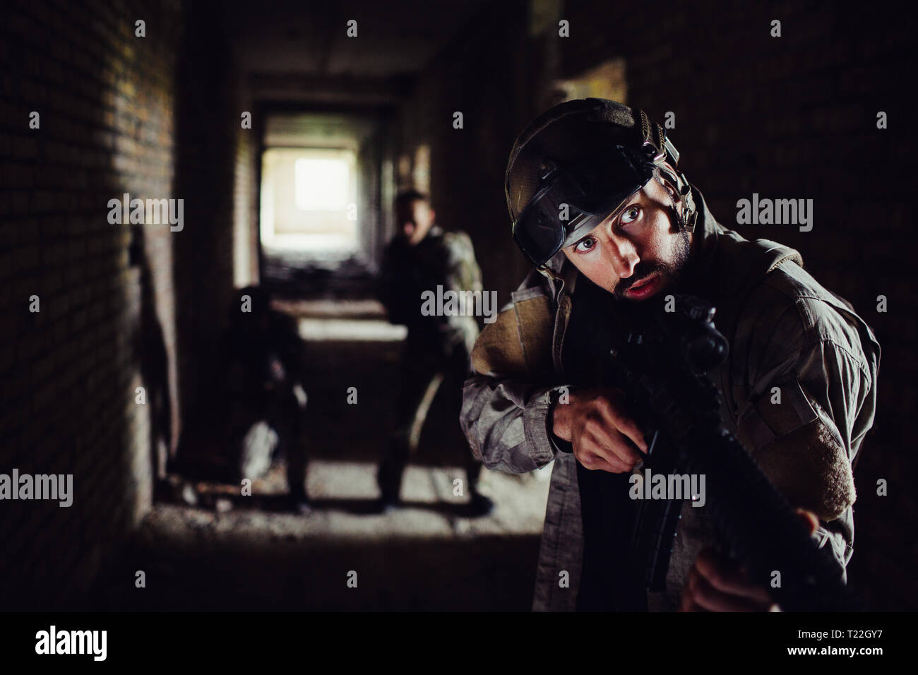 Drei Soldaten stehen in dunklen Flur und wartet. Der Kerl vor ist auf der Suche nach rechts und Halten der Waffe in der Hand. Die anderen zwei sind s Stockfoto