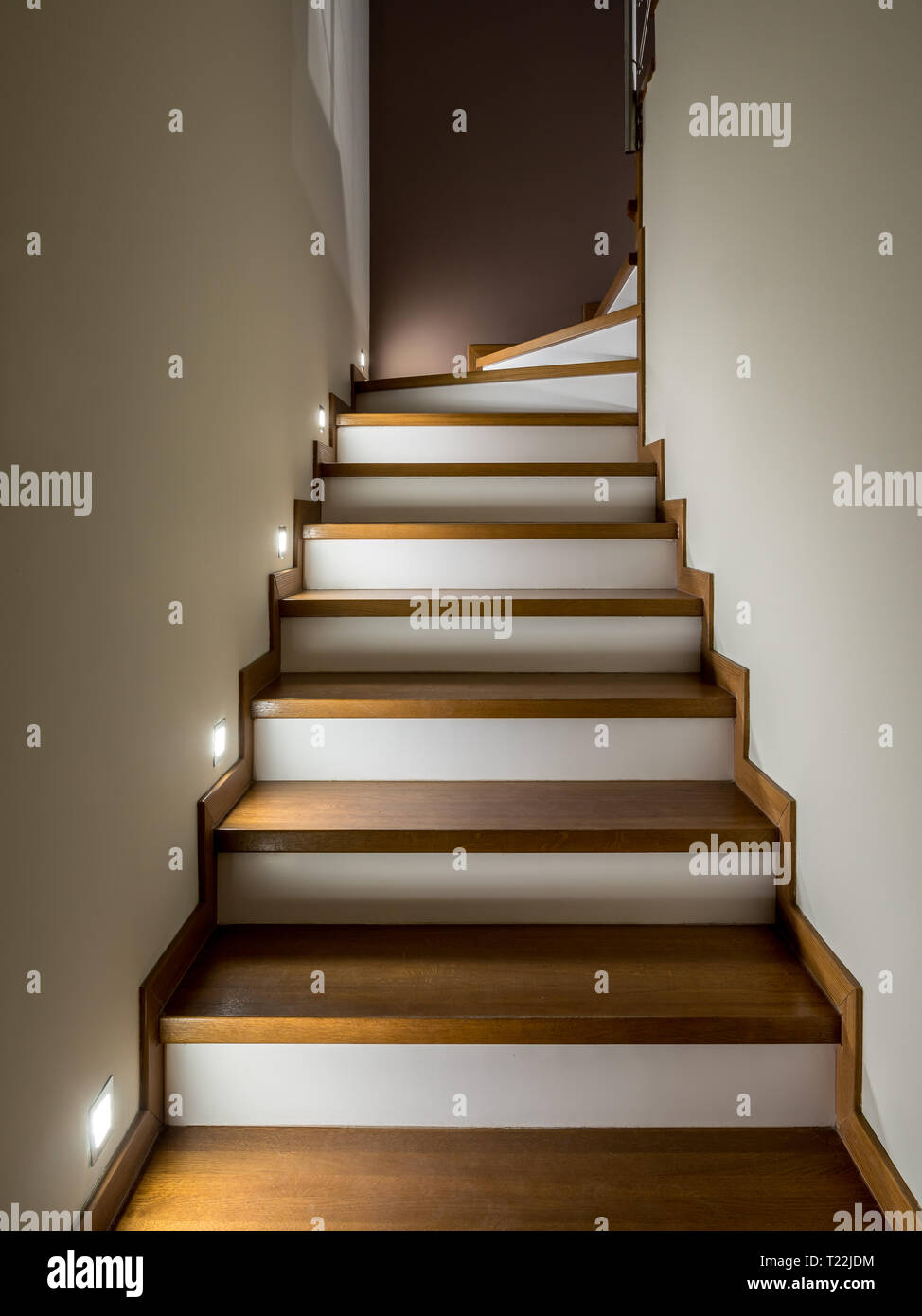 Beleuchtete Treppe mit Holzstufen und weißen Setzstufen - eine moderne Innenausstattung Stockfoto
