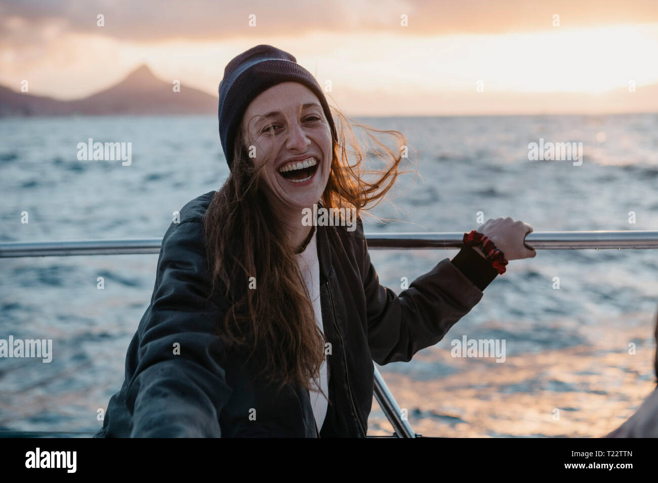 Südafrika, junge Frau mit wollmütze während der Bootsfahrt bei Sonnenuntergang lachen Stockfoto