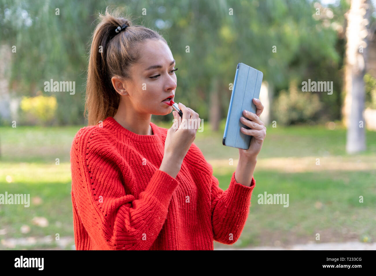 Junge Frau Anwendung Lippenstift in apark, mit digitalen Tablet als Spiegel Stockfoto