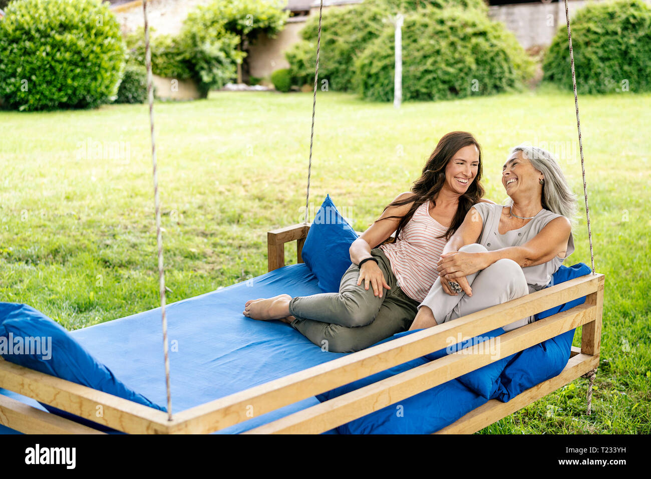 Zwei glückliche Frauen entspannen auf ein hängendes Bett im Garten Stockfoto