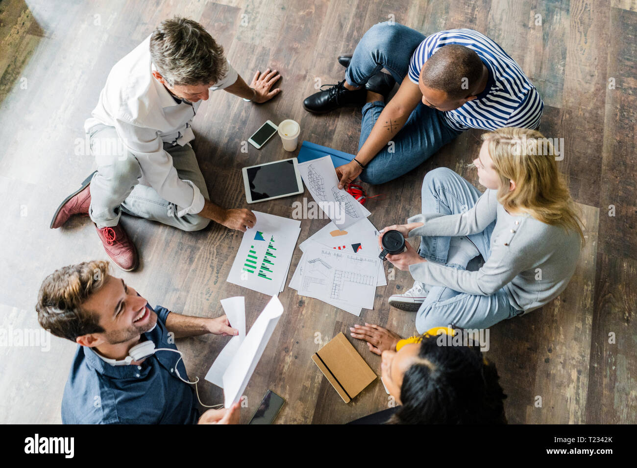 Happy Business Team sitzen auf dem Boden diskutieren Dokumente in loft Büro Stockfoto