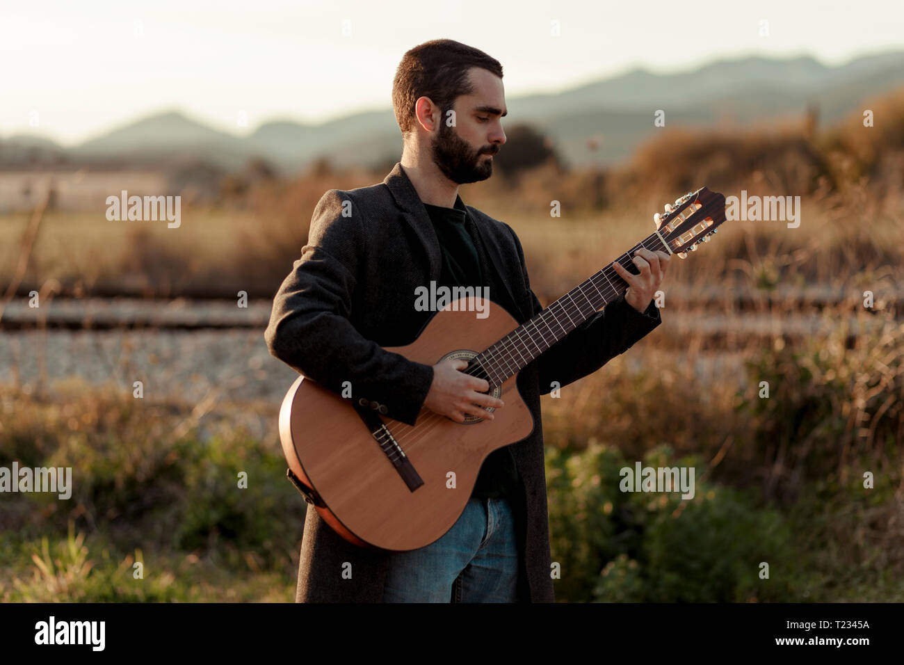 Männliche Musiker mit Bart spielt die Gitarre in der Landschaft Stockfoto
