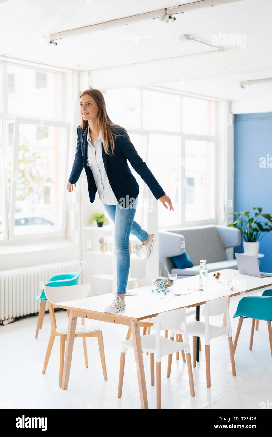 Junge Geschäftsfrau auf ein Bein auf dem Schreibtisch im Zimmer Stockfoto