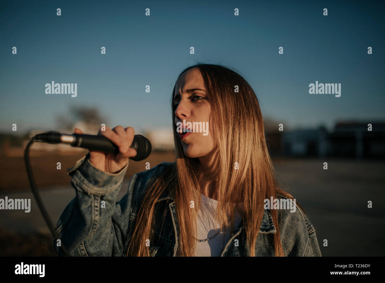 Junge Frau Singen mit einem Mikrofon im Freien Stockfoto