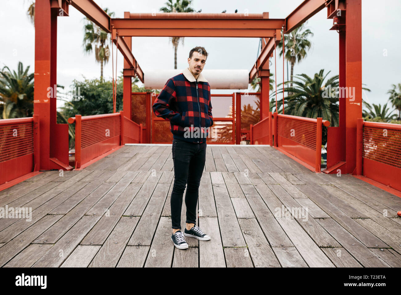 Junger Mann mit legere Kleidung auf einem roten Brücke an Kamera suchen Stockfoto