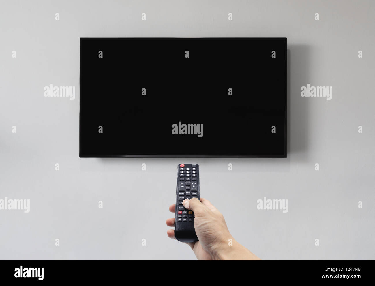 Fernsehen auf weiße Wand mit Hand mit Fernbedienung, leeren schwarzen Bildschirm Stockfoto