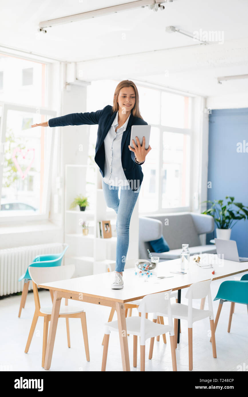 Junge Geschäftsfrau auf ein Bein auf dem Schreibtisch im Zimmer, halten digitale Tablet Stockfoto