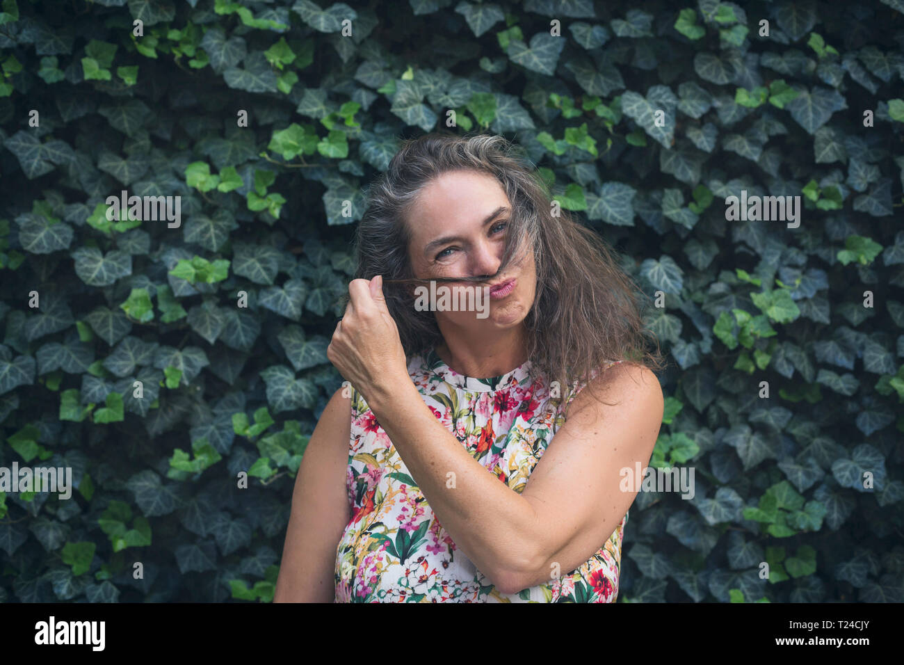 Portrait von reife Frau stand vor der Wand mit Efeu bewachsene schmollen Mund Stockfoto