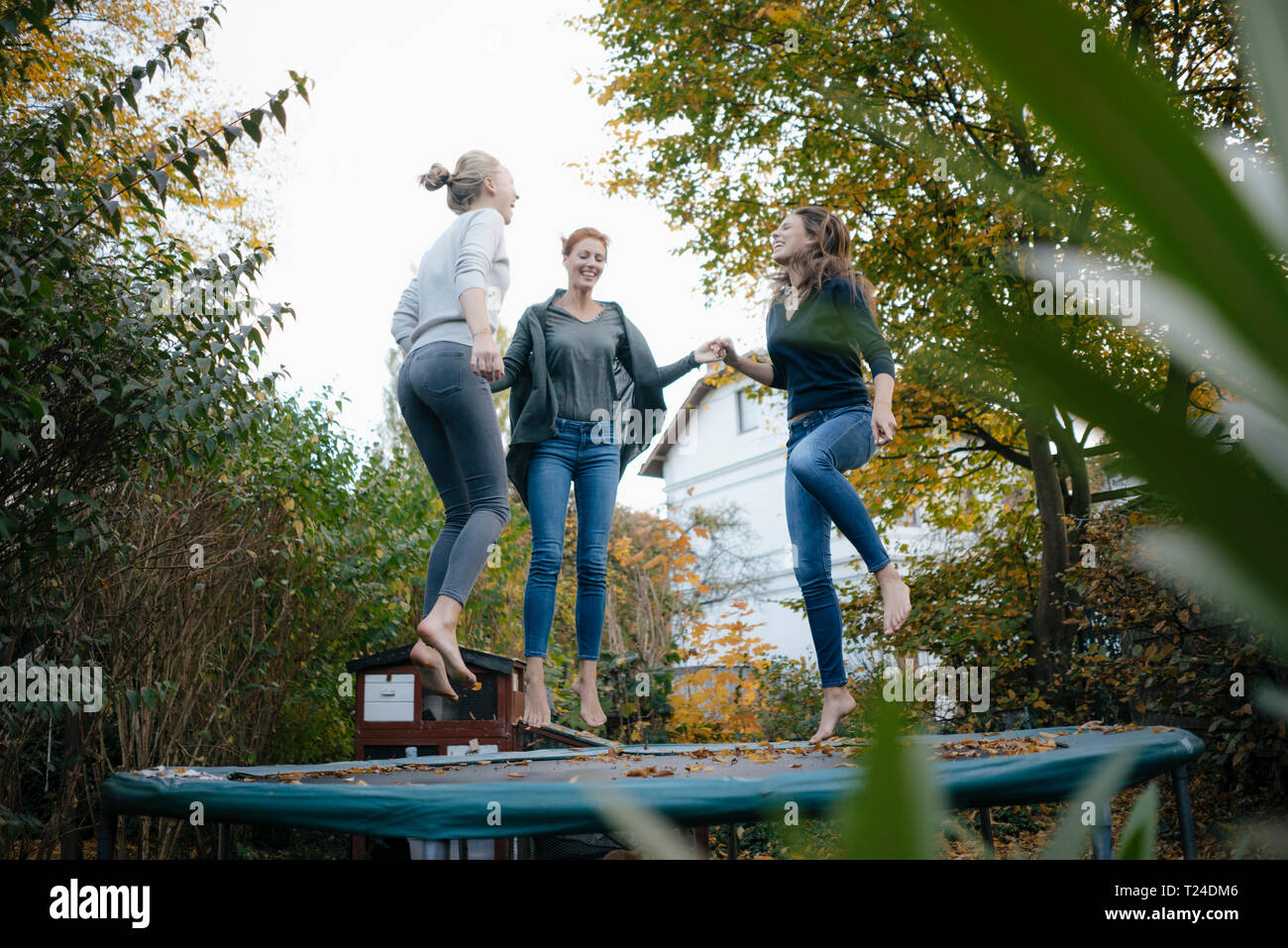 Glückliche Mutter mit zwei Töchtern im Teenageralter springen auf Trampolin im Garten im Herbst Stockfoto