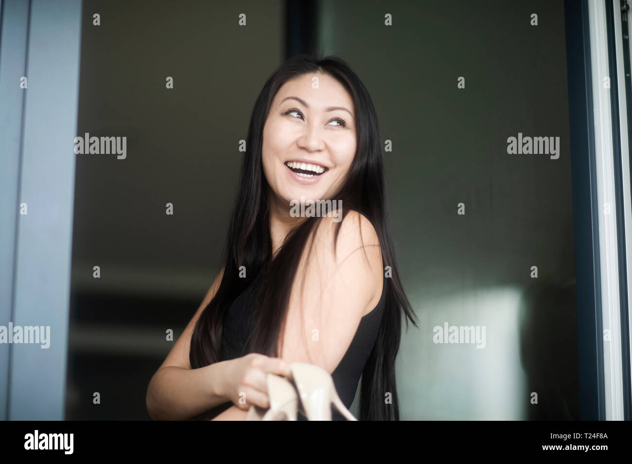 Glückliche junge Frau im schwarzen Kleid mit High Heels am Fenster Stockfoto
