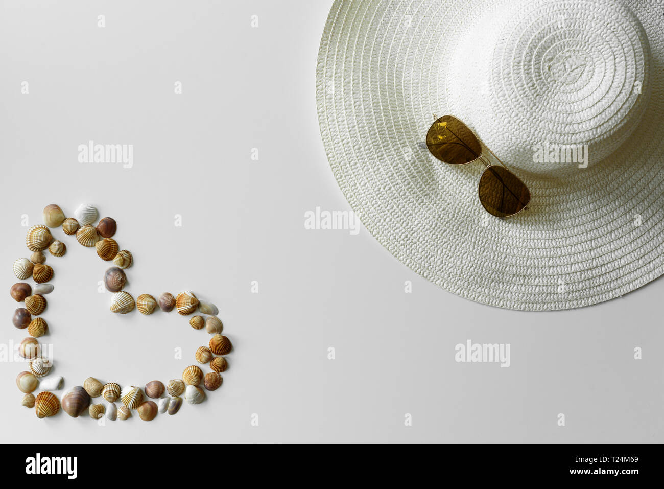 Romantische Sommer Dekoration. Herz aus Muscheln und Sonnenhut mit Aviator Sonnenbrille auf weißem Hintergrund eingerichtet. Stockfoto