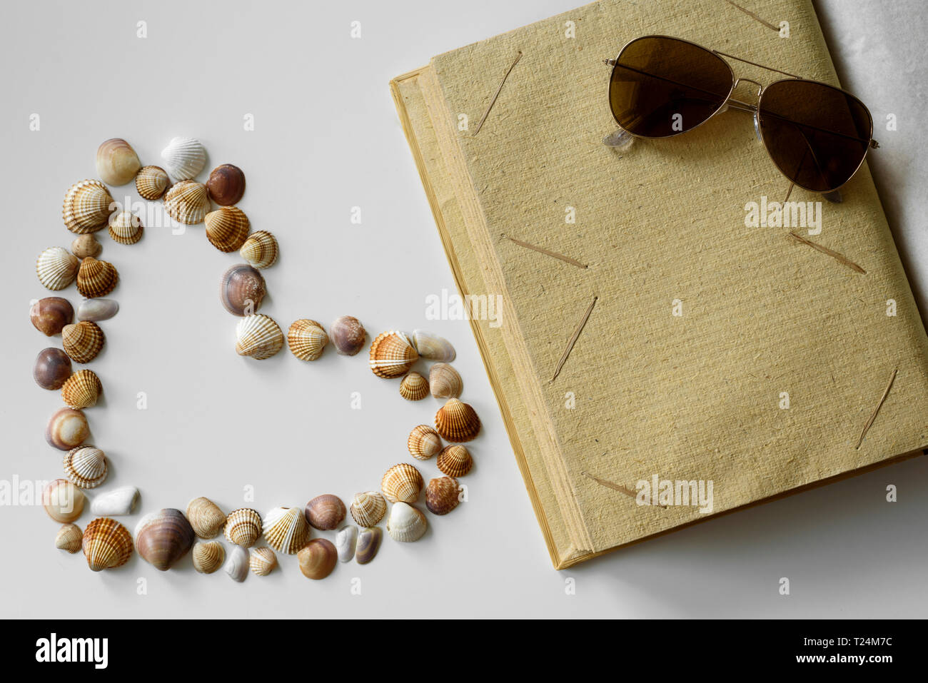 Sommer mit Herzförmigen seashells konzipiert, leere Papier Fotoalbum und braun Pilotenbrillen. Stockfoto
