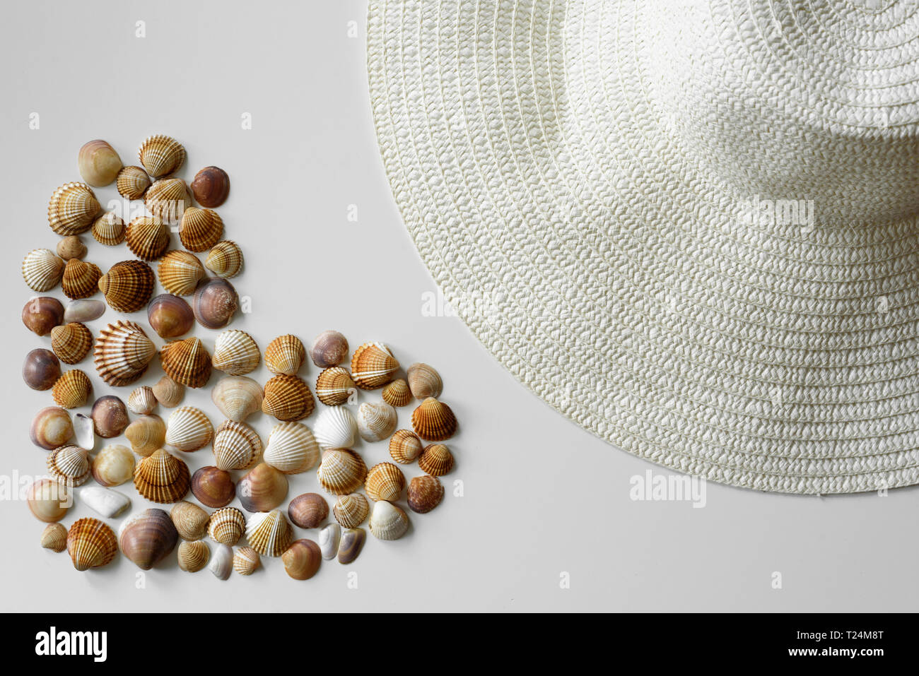 Minimalistischer Sommer Dekoration aus Muscheln bilden einen vollen Herzen und Stroh Sonnenhut auf weißem Hintergrund erstellt. Stockfoto