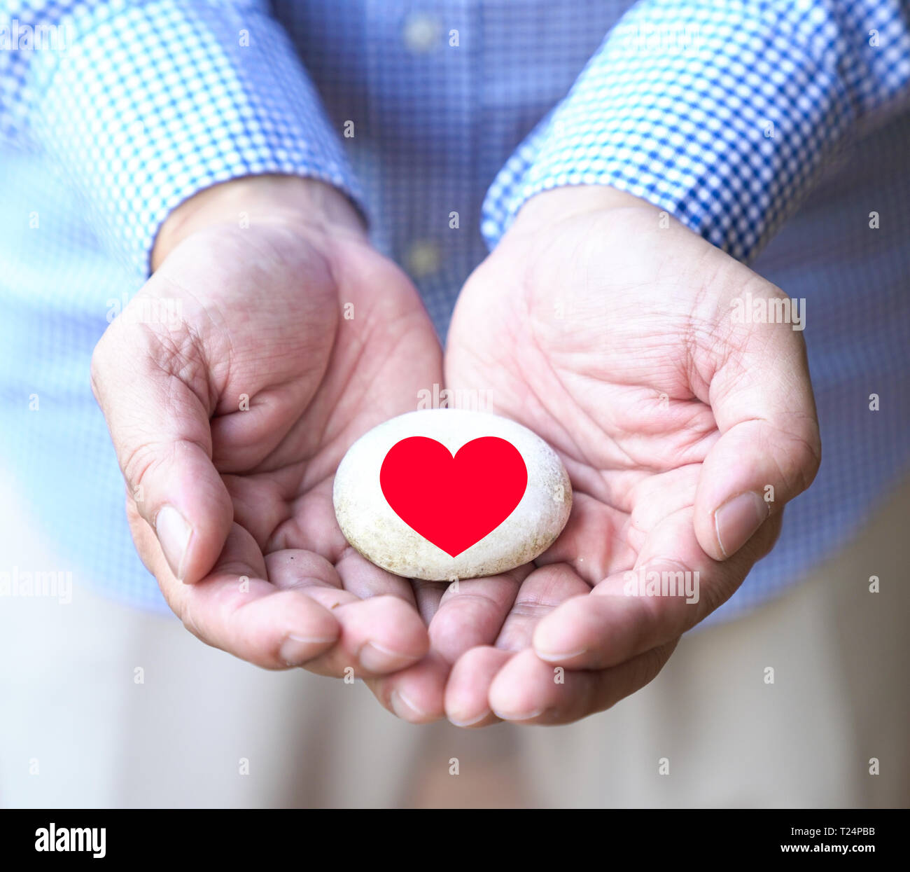 Liebe oder schützen das Herz Konzept. Hände schröpfen einen Kieselstein mit roten Herzen bedruckt Stockfoto