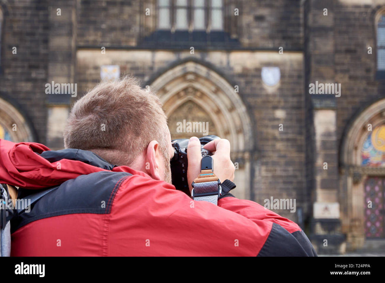 Mann im roten Mantel und mit Rucksack auf dem Rücken, Kamera und Fotos von alten Gebäude Stockfoto