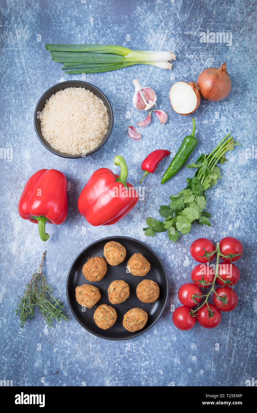 Bestandteile einer falafel jambalaya Rezept. Blick von oben auf die Reis in einem dunklen Schüssel, falafels auf einem dunklen Platte, Tomaten, corianders, Chili, Paprika, auf Stockfoto