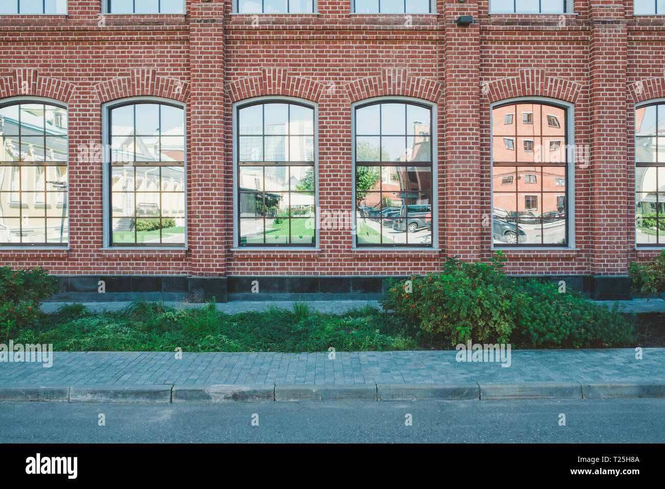 Bürogebäude im Loft-Stil. Große Fenster. Red brick wall. Grüne Büsche auf der Mitte. Flache Fassade Zusammensetzung Stockfoto