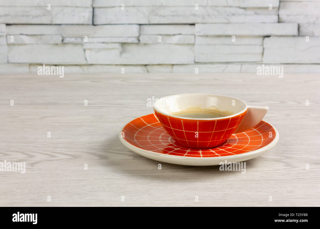 Orange Tasse Kaffee mit einem modernen Design auf einem weißen Tisch Stockfoto