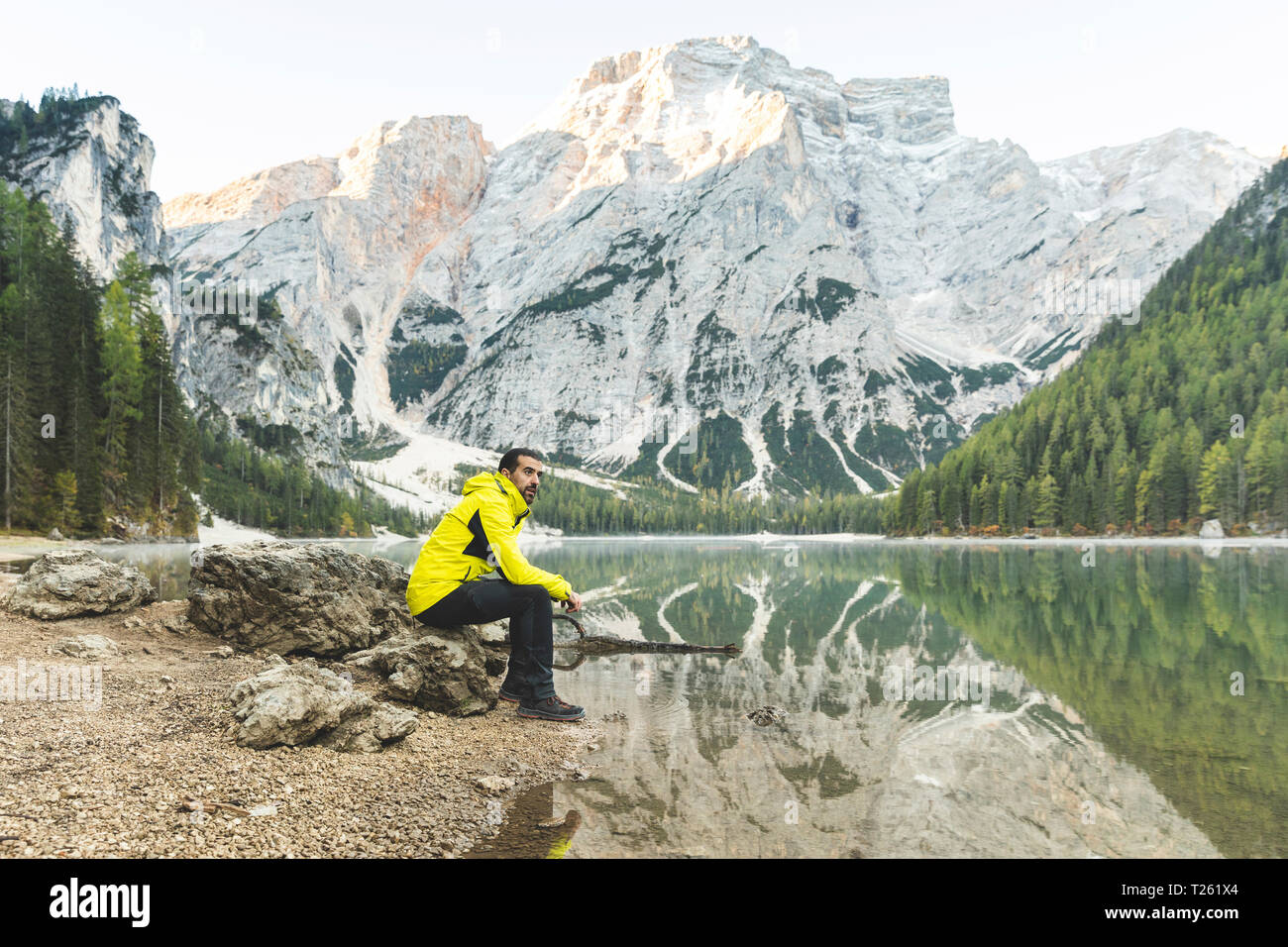 Italien, Pragser See, Mann sitzt auf einem Felsen am See mit Berge und Wald im Hintergrund Stockfoto