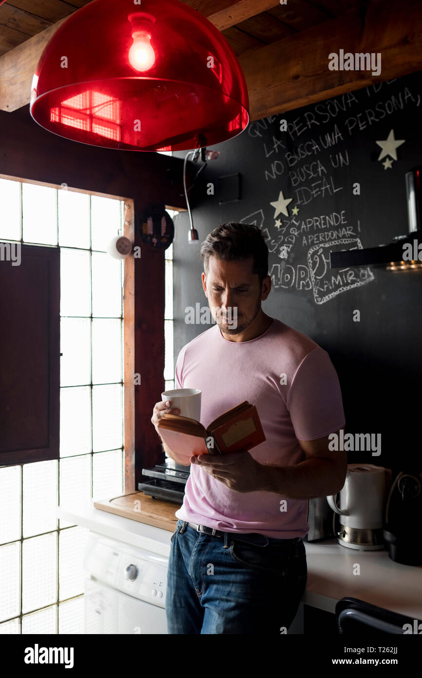 Mann mit Tasse Kaffee ein Buch lesen in der Küche Stockfoto