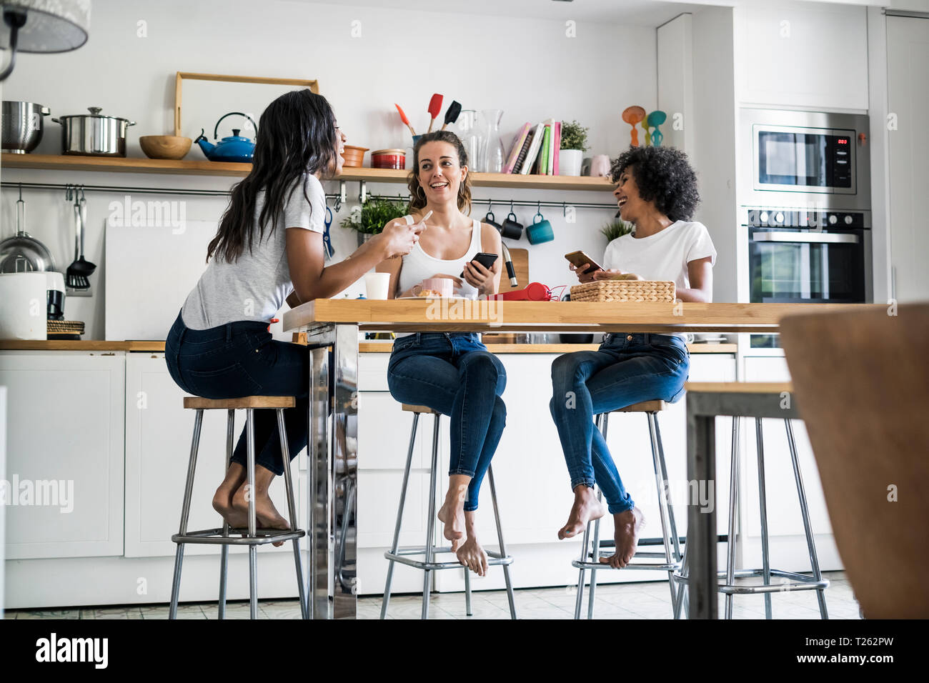 Drei glückliche Frauen am Küchentisch zu Hause sitzen sozialisieren Stockfoto