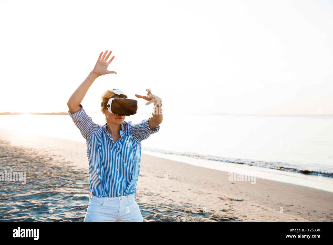 Blonde Frau tun Art von Yoga Übungen auf einem Strand in Thailand mit 3D Virtual Reality goggles Stockfoto